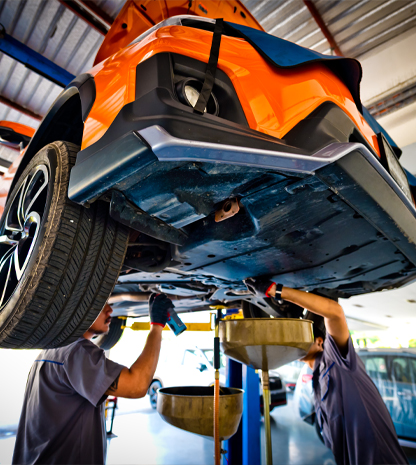 Two car mechanics working on underneath of car on lift